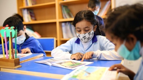 image of three elementary-age students wearing masks reading books